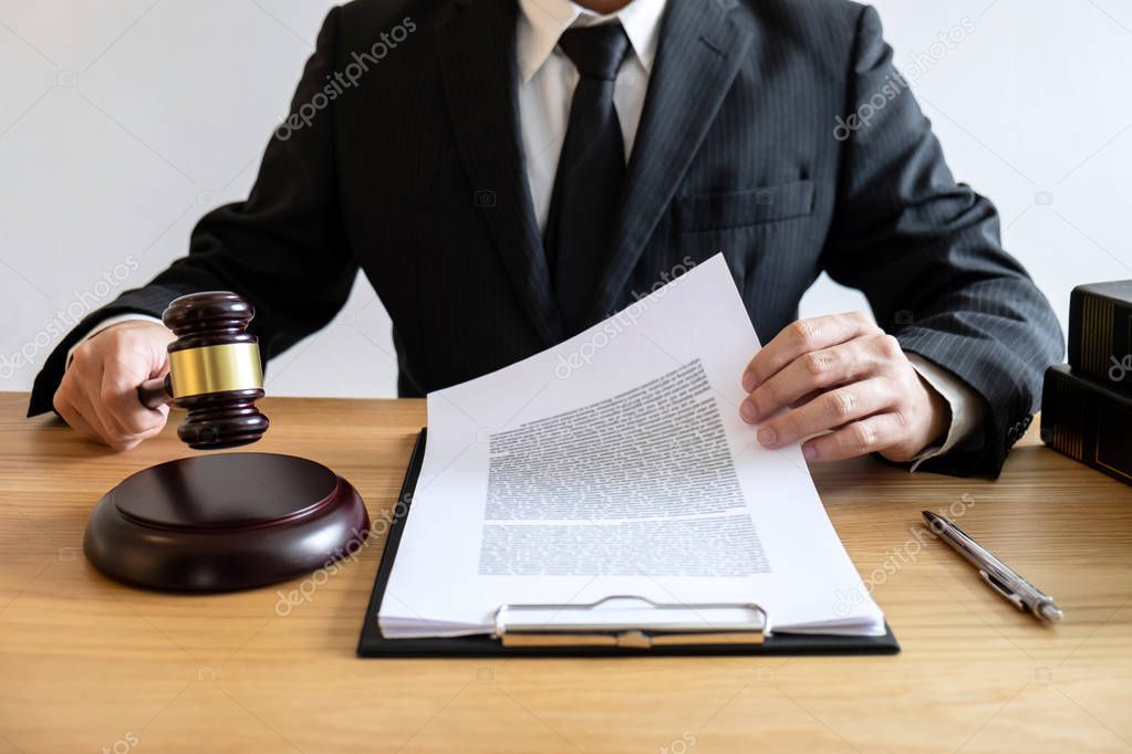 Legal law, advice and justice concept, male counseling lawyer or notary working on a documents and contract papers of the important case and wooden gavel, brass scale in courtroom.