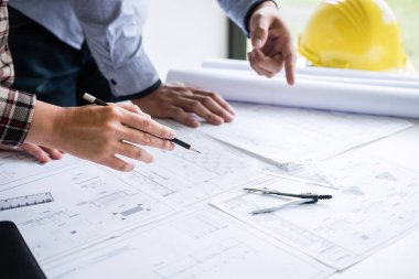 İnşaat mühendisi veya mimar, çalışma sahasındaki mimari projenin çizim ve çizim toplantısına ilişkin bilgileri incelerken bir planı da tartışır..