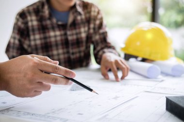 İnşaat mühendisi veya mimar, çalışma sahasındaki mimari projenin çizim ve çizim toplantısına ilişkin bilgileri incelerken bir planı da tartışır..