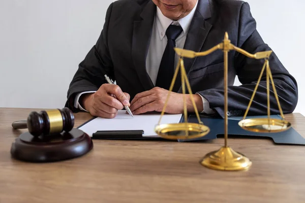 Legal law, advice and justice concept, counselor lawyer or notary working on a documents and report of the important case and wooden gavel, brass scale on table in courtroom.