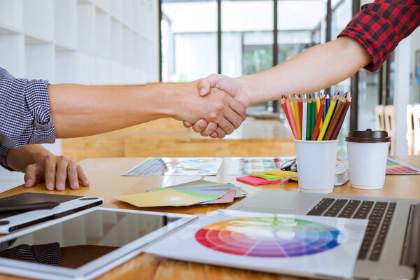 Cooperation of Young creative graphic designer working on workspace and shaking hands after successful of new project, putting hands together.