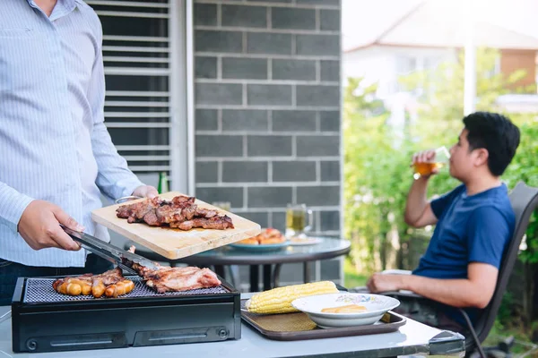 Group of friends Two young man enjoying grilled meat and raise a — Stock Photo, Image