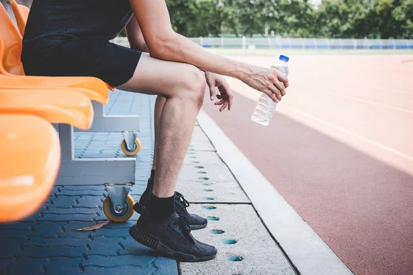 Joven atleta de fitness hombre descansando en el banco con botella de agua — Foto de Stock