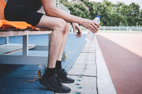 Joven atleta de fitness hombre descansando en el banco con botella de agua — Foto de Stock