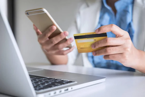 Joven consumidor sosteniendo teléfono inteligente, tarjeta de crédito y mecanografía — Foto de Stock