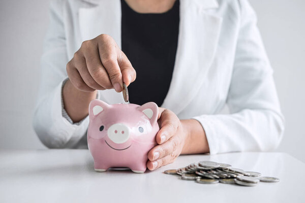 Business woman putting coin into pink piggy bank for planning st