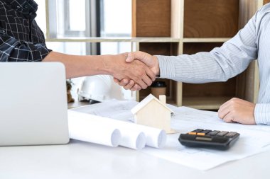 İşbirliği, inşaat mühendisliği veya mimarın el sıkışması, ortakların çizim, mimari proje toplantısı hakkındaki bilgileri incelerken bir plan ve inşa modelini tartışır.