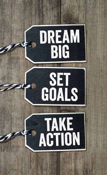 Black wooden hang tag with dream big, set goals and take action on wooden background