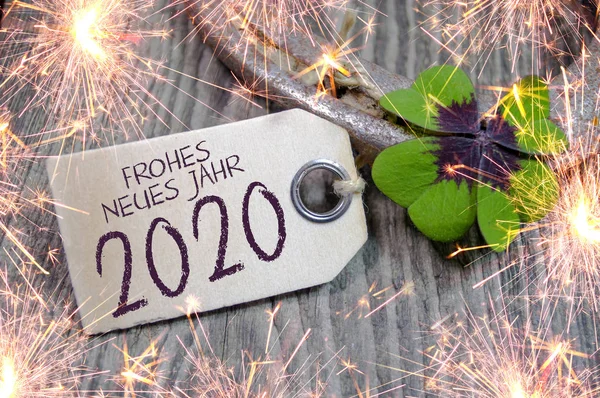 Wooden hang tag with four leaf clover and sparklers with happy new year 2020 on wooden weathered background