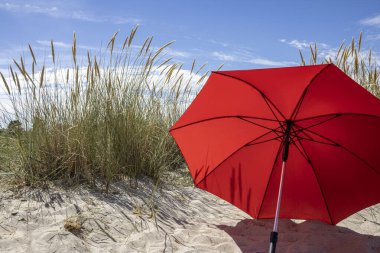 Kumda kırmızı kumsal şemsiyesi Mavi yaz gökyüzü ile kum tepeleri arasında 