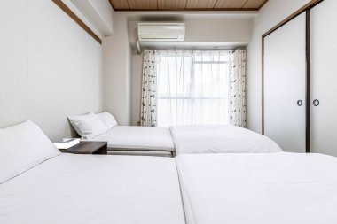 Japon tarzı bir evde küçük beyaz bir yatak odasında ikiz yataklar ve beyaz battaniyeler.