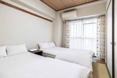 Japon tarzı bir evde küçük beyaz bir yatak odasında ikiz yataklar ve beyaz battaniyeler.