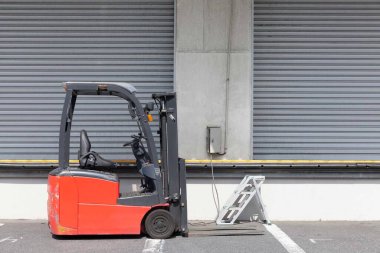 Endüstriyel bölgedeki bir deponun önüne bir forklift park edilmiş.