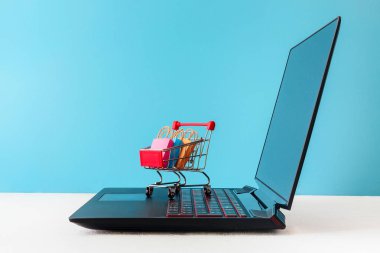 Interneinternet dükkanı / e-ticaret satış ve teslimat hizmeti kavramı: alışveriş sepeti çok renkli paketleri ve kutuları laptop klavye, mavi zemin üzerine troleybüs logolu