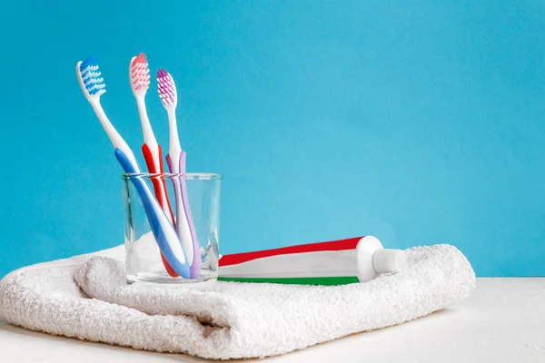 Healthy teeth. Toothbrushes in a glass and toothpaste and bath towel on a table in the bathroom on a blue background. Design, health care, hygiene health and fresh breath