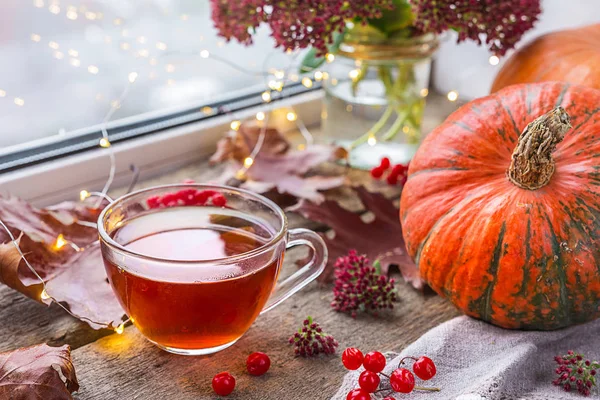 Life style of comfort in the autumn. A cup of tea in the living room on the table by the window with raindrops, autumn leaves and pumpkin, the concept of comfort and interior