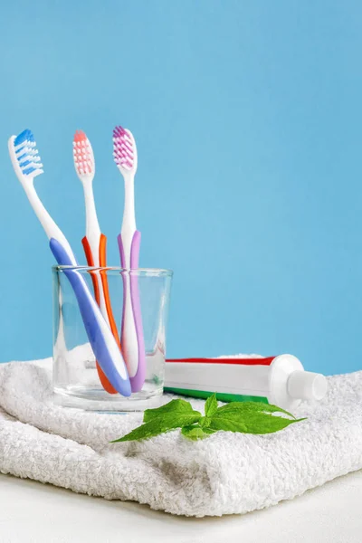 Healthy teeth. Toothbrushes in a glass and toothpaste and mint leaves a bath towel on the table in the bathroom on a blue background. Design, health care, hygiene health and fresh breath