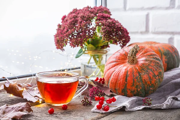 Life style of comfort in the autumn. A cup of tea in the living room on the table by the window with raindrops, autumn leaves and pumpkin, the concept of comfort and interior