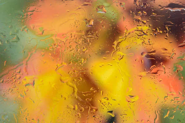 Autumn background. Drops of rain on the wet window and autumn colors of red orange and yellow. Blurred abstract texture background.