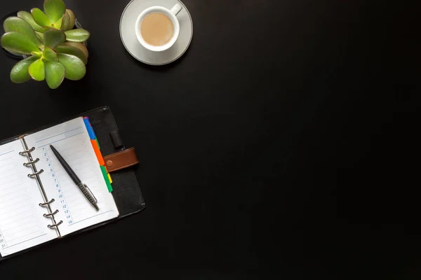 High angle view of office black desk with copy space. Table with keyboard, computer, coffee cup and supplies. Top view of blackboard office desk. Businessman or student desk.