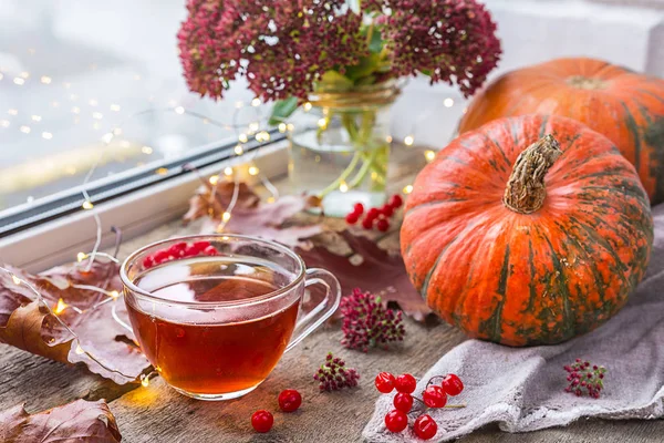Life style of comfort in the autumn. A cup of tea in the living room on the table by the window with raindrops, autumn leaves and pumpkin, the concept of comfort and interior