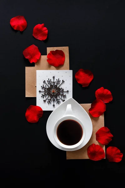 White cup of coffee on a black background with rose petals with copy space, flat lay top view. Art trend glamor romantic style