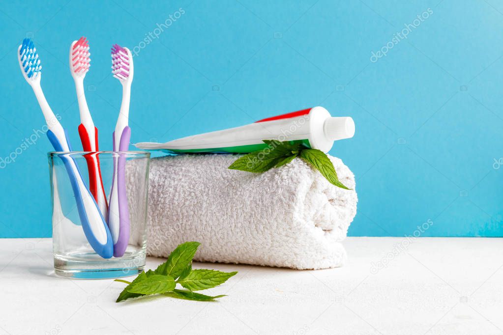Healthy teeth. Toothbrushes in a glass and toothpaste and mint leaves a bath towel on the table in the bathroom on a blue background. Design, health care, hygiene health and fresh breath