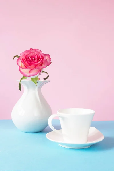 White cup and pink rose in vase on table