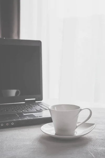 cup of coffee and a laptop on a table near a window in Scandinavian style minimalism in gray with a copy space