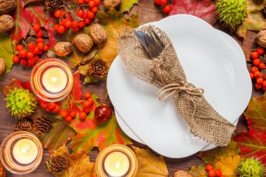 Sofra - tabak ve sonbahar yaprakları, rowan çilek, kestane, ceviz ve mumrustik tarzı, sonbahar kavramı ile dekore edilmiş ahşap bir masada bir bıçak ile bir çatal seti