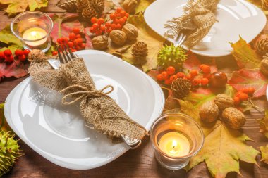 Sofra - tabak ve çatal ile sonbahar dekore edilmiş ahşap bir masa üzerinde bir bıçak ile bir dizi yaprakları, üvez meyveleri, kestane, ceviz ve mumlar, rustik tarzda sonbahar kavramı