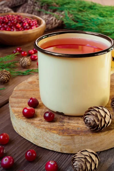 Drink juice from cranberries in an iron cup on a dark background with spruce branches and cones with copy space concept of cold and warming medicinal drinks
