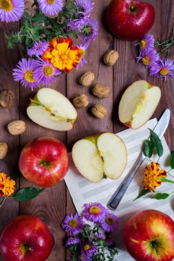 Kırmızı elma ve mor ve sarı çiçekler, bıçak ve ahşap bir arka plan üzerinde notlar dilimleri, sabah sonbahar günü atmosferi ve melodiler
