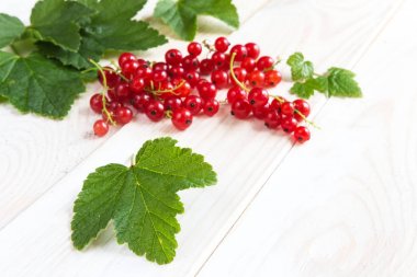 Sulu kırmızı frenk üzümü meyveleri ve hafif ahşap bir arka plan üzerinde yaprakları. Kopyalama alanı ile desen düz yatıyordu