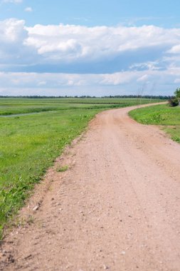 Bir yaz gününde bulutlar ile mavi bir gökyüzüne karşı alanın ortasında uzun kumlu yol