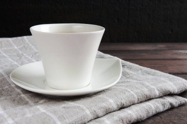 Beyaz kupa ve masa örtüsü koyu bir tahta masada.