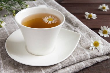 Sağlıklı bitkisel içecek kavramına sahip koyu ahşap bir masa üzerinde papatya çayı serpiştirilmiş beyaz bardak.