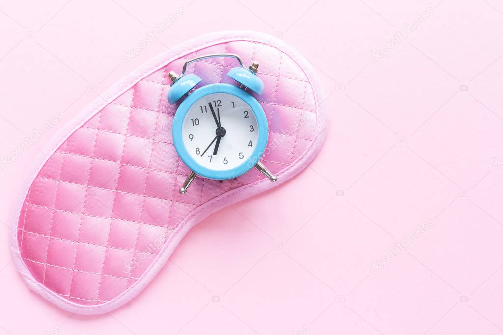 Sleeping eye mask, alarm clock isolated on pink pastel colourful trendy background. Do not disturb me, let me sleep. Rest, good night, siesta, insomnia, relaxation, tired, travel concept