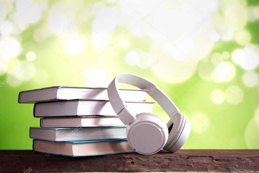 old books with headphones on wooden table on green background