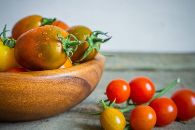Sebzeler. Taze domates çeşitlerinden oluşan bir kompozisyon ve ahşap arka planda bir kasede fotokopi alanı olan yapraklar..