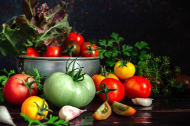 Taze domatesler, maydanoz, dereotu, sarımsak koyu bir arka planda, kırsal bir mutfakta ve ahşap çatallar.