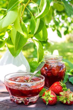 Çilek reçeli ve sulu olgun çilekler bahçedeki ahşap bir masanın üzerinde güneşli bir yaz akşamında, kırsal bir tarzda, bahçecilik, sağlıklı organik vitamin besin konsepti