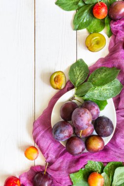 Beyaz ahşap arkaplan deseni üzerinde sulu erikler ve mor çalıştırıcı metin düz üst görünümü için kopya alanı ile