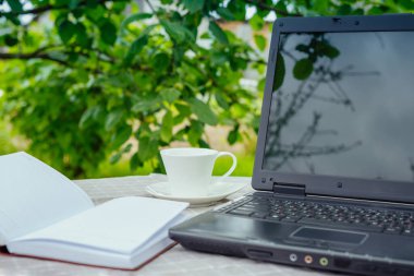 Çay, dizüstü bilgisayar, bir bilgisayar, bir yaz sabahı bahçede bir kitap parlatma masası çalışmak için bir yer, serbest çalışma konsepti. 