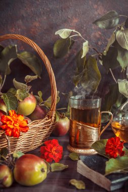 Bardakta elma çayı, sürahi ve olgun elmalarla dolu bir sepet eski usul ahşap bir masada.