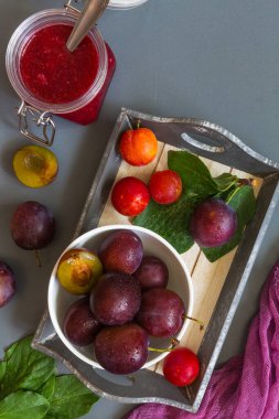 Beyaz çatal bıçaklarda sulu kırmızı erikler ve erik reçeli ve gri lakonik arkaplan deseninde mor koşucu ve metin düz görünümü için fotokopi alanı yatar