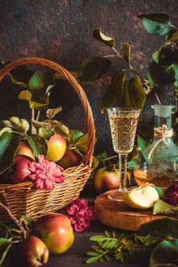 Bardakta elma şarabı, sürahi ve sepet içinde olgun elmalar eski usul ahşap bir masada.