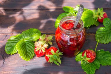 Çilek reçeli ve sulu olgun çilekler bahçedeki ahşap bir masanın üzerinde güneşli bir yaz akşamında, kırsal bir tarzda, bahçecilik, sağlıklı organik vitamin besin konsepti