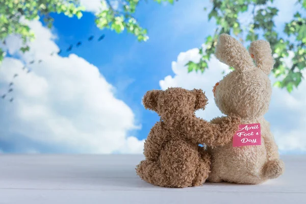 Two friends of the toy bears are sitting on the boards against the background of the summer sky on April Fool's Day with a sticker on the back, humor, a joke — Stock Photo, Image