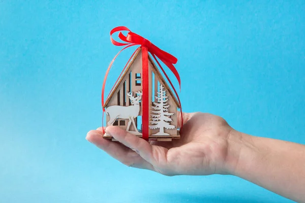 Γυναίκα χέρι κρατώντας ένα σπίτι μοντέλο και ένα κουτί δώρου δεμένο με μια κόκκινη κορδέλα σε μπλε φόντο για την αγορά ενός νέου σπιτιού ή ακινήτων για μια οικογένεια ή άτομο μια αγαπημένη έννοια. — Φωτογραφία Αρχείου